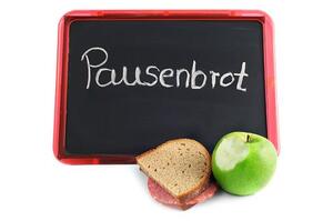 "packed lunch with letters Pausenbrot (German, packed lunch) on blackboard. brown bread with apple"